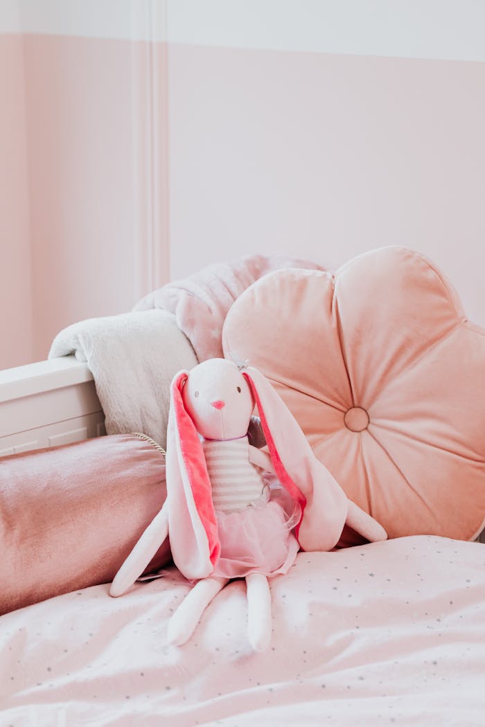 Cute pink stuffed bunny sits on a cozy, soft pink bed with pillows. Ideal for childrens room inspiration.